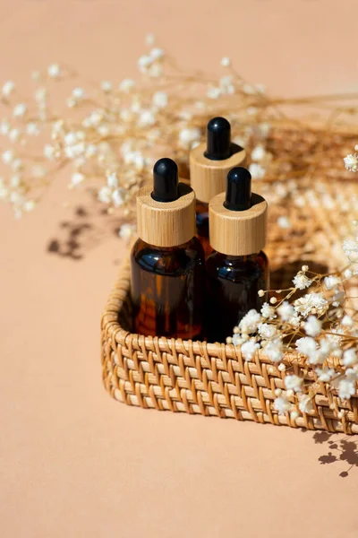 Amber bottles with dropper pipette in a wicker basket. Beige background with daylight and beautiful shadows. Skincare serum or essential oil natural cosmetic. Beauty concept for face and body care