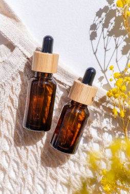 Kehribar şişe damlası pipeti, serum ya da gerekli yağ ve bez torbası, güzel bir tarla çimeni. Beyaz arka plan, gün ışığı ve gölgeler. Yüz bakımı için güzellik konsepti