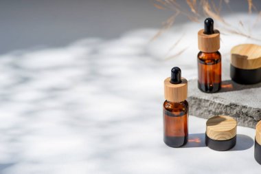 Bambu kapaklı ve siyah kavanozlu kehribar cam damlası. Ürün sunumu için gri beton podyumda bir şişe. Cilt bakım ürünleri ve kır çiçekleri. Güzellik konsepti