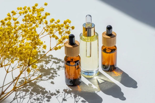 Transparent and amber bottles with dropper pipette with serum or essential oil with beautiful yellow flowers. White background with daylight and beautiful shadows. Beauty concept for face body care