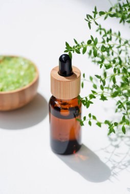 Kehribar şişesinde damla pipeti ve serum ya da kekik yağı var. Beyaz arka plan, gün ışığı ve güzel gölgeler. Cilt bakım ürünleri, doğal kozmetik ürünleri. Yüz ve vücut bakımı için güzellik konsepti