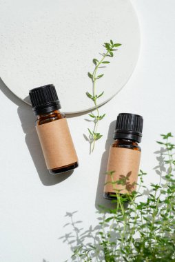 Zanaat etiketli kehribar şişeleri gerekli yağ ve yeşil kekik dalları. Beyaz arka plan, gün ışığı ve güzel gölgeler. Cilt bakım ürünleri, doğal kozmetik ürünleri. Yüz ve vücut bakımı için güzellik konsepti