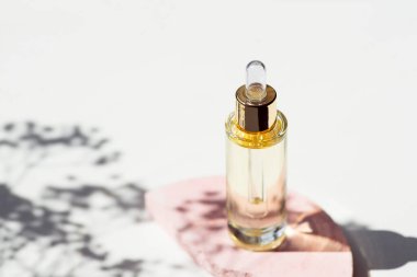 Serumlu damlalık pipetli şeffaf şişe ya da çiçek gölgeli pembe beton podyumda gerekli yağ. Gündüz vakti beyaz arka plan. Yüz ve vücut bakımı için güzellik konsepti