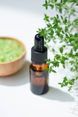 Kehribar şişesinde damla pipeti ve serum ya da kekik yağı var. Beyaz arka plan, gün ışığı ve güzel gölgeler. Cilt bakım ürünleri, doğal kozmetik ürünleri. Yüz ve vücut bakımı için güzellik konsepti