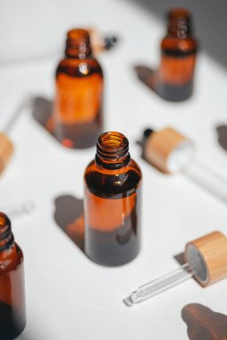 Kehribar, mavi ve şeffaf şişeler serumla kaplanmamış ya da beyaz çiçeklerle yağlanmamış. Bej arka plan, gün ışığı ve güzel gölgeler. Yüz ve vücut bakımı için güzellik konsepti