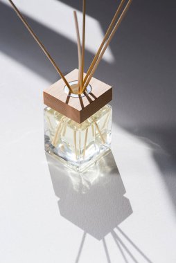 Beyaz arka planda şeffaf aroma yayıcı şişesi. Ev yapımı sunum için parfüm. Moda konsepti. Sarı sıvı ve ahşap kaplama