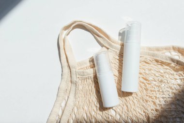 Krem ya da losyon için plastik beyaz tüpler ve bez alışveriş çantası. Beyaz arka planda güneş kremi kozmetiği. Yüz bakımı için güzel yaz konsepti