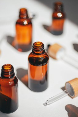 Kehribar, mavi ve şeffaf şişeler serumla kaplanmamış ya da beyaz çiçeklerle yağlanmamış. Bej arka plan, gün ışığı ve güzel gölgeler. Yüz ve vücut bakımı için güzellik konsepti