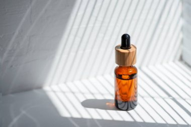 Şişede damla pipeti ve serum ya da gerekli yağ var. Beyaz arka plan, gün ışığı ve güzel köşegen gölgeler. Cilt bakım ürünleri, doğal kozmetik ürünleri. Yüz ve vücut bakımı için güzellik konsepti