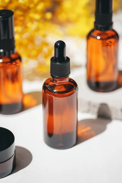 Amber dropper bottles with serum, tonic or essential oil on grey concrete podium with yellow flowers.White background with daylight. Beauty concept for face and body care