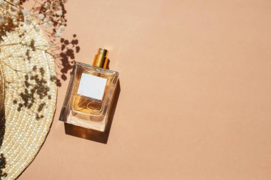 Transparent bottle of perfume with label. Cloth shopping bag and sun hat on beige background. Fragrance presentation with daylight. Trending concept in natural materials with yellow field flowers. Women's and men's essence.