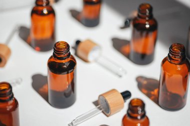 Kehribar, mavi ve şeffaf şişeler serumla kaplanmamış ya da beyaz çiçeklerle yağlanmamış. Bej arka plan, gün ışığı ve güzel gölgeler. Yüz ve vücut bakımı için güzellik konsepti