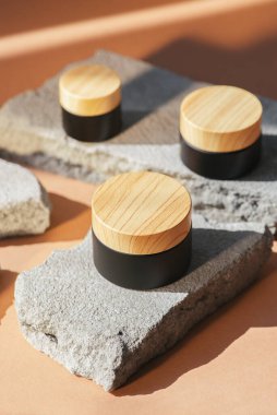 Ürün sunumu için gri beton podyumda krem ya da losyonlu siyah kozmetik kavanoz ahşap kapağı. Cilt kozmetiği. Günışığı ve gölgeli bej bir arka plan. Yüz bakımı için güzellik konsepti