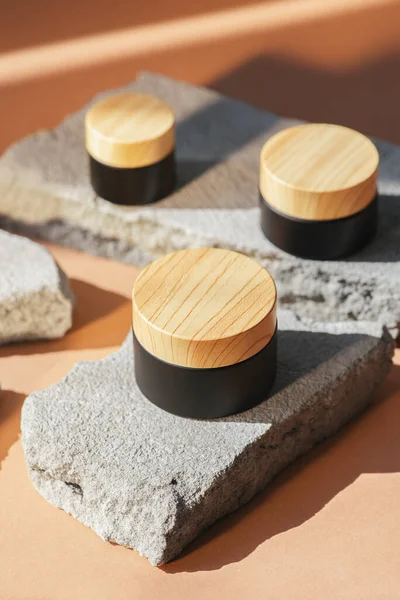 Ürün sunumu için gri beton podyumda krem ya da losyonlu siyah kozmetik kavanoz ahşap kapağı. Cilt kozmetiği. Günışığı ve gölgeli bej bir arka plan. Yüz bakımı için güzellik konsepti