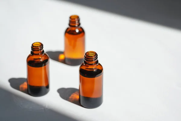 Open amber bottle with serum or essential oil. White background with daylight and beautiful shadows. Beauty concept for face and body care