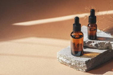 Siyah kapaklı ve kuru bitkili kehribar cam damlası. Ürün sunumu için gri beton podyumda şişeler. Cilt bakım ürünleri ve kır çiçekleri. Güzellik konsepti