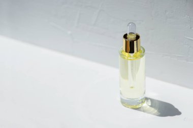 Damla pipetli şeffaf bir şişe serum ya da gerekli yağ. Beyaz arka plan, gün ışığı ve güzel gölgeler. Cilt bakım ürünleri, doğal kozmetik ürünleri. Yüz ve vücut bakımı için güzellik konsepti