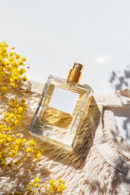 Beyaz arka planda etiketi ve kumaş alışveriş çantası olan şeffaf bir parfüm şişesi. Gün ışığıyla güzel kokulu bir sunum. Doğal malzemelerde sarı tarla çiçekleriyle moda olan bir kavram. Kadın ve erkeğin özü..