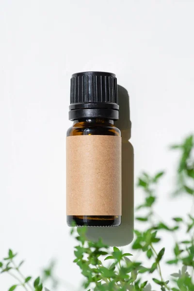 Amber bottle with craft label thyme essential oil. White background with daylight and beautiful shadows. Skincare products, natural cosmetic. Beauty concept for face and body care