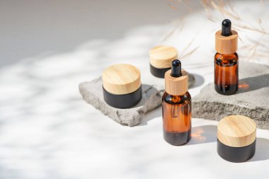 Bambu kapaklı ve siyah kavanozlu kehribar cam damlası. Ürün sunumu için gri beton podyumda bir şişe. Cilt bakım ürünleri ve kır çiçekleri. Güzellik konsepti