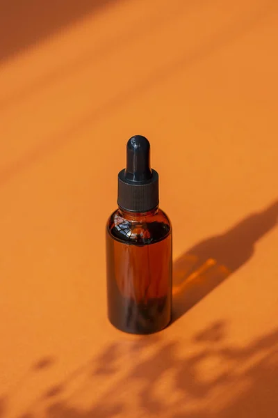 Amber bottle with dropper pipette with serum or essential oil. Orange background with daylight and beautiful shadows. Skincare products, natural cosmetic. Beauty concept for face and body care