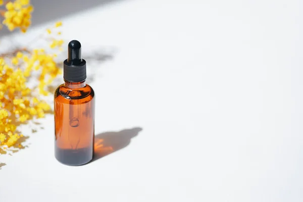 Amber dropper bottles with serum, tonic or essential oil with yellow flowers. White background with daylight. Beauty concept for face and body care