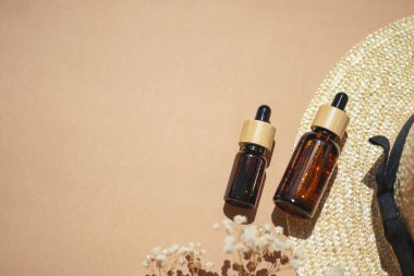 Sarı pipeti ve bej arka planda güneş şapkası olan kehribar şişesi. Doğal malzemelerde tarla çiçekleriyle moda olan bir kavram. Cilt serumu ya da doğal yağ kozmetiği. Yüz ve vücut bakımı için güzellik konsepti