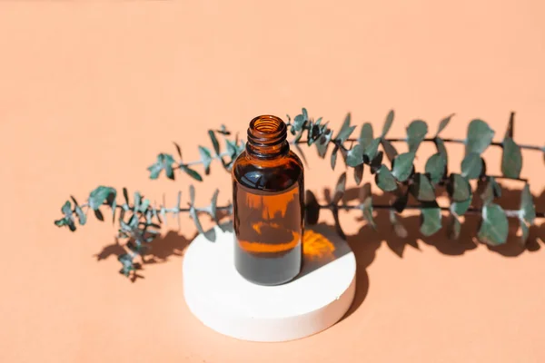 Open amber bottle without cap with eucalyptus branches. Beige background with daylight and beautiful shadows. Skincare serum or essential oil natural cosmetic. Beauty concept for face and body care