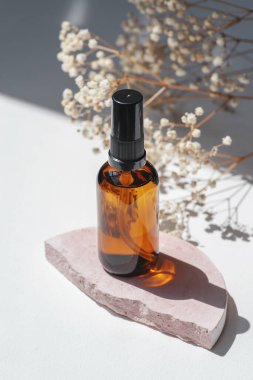 Kehribar şişesinde serum, tonik ya da esaslı yağ var. Pembe beton podyumda. Beyaz arka plan, gün ışığı ve kır çiçekleri. Yüz ve vücut bakımı için güzellik konsepti