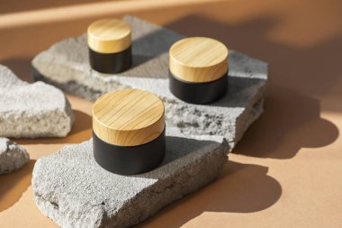 Ürün sunumu için gri beton podyumda krem ya da losyonlu siyah kozmetik kavanoz ahşap kapağı. Cilt kozmetiği. Günışığı ve gölgeli bej bir arka plan. Yüz bakımı için güzellik konsepti