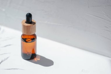 Şişede damla pipeti ve serum ya da gerekli yağ var. Beyaz arka plan, gün ışığı ve güzel gölgeler. Cilt bakım ürünleri, doğal kozmetik ürünleri. Yüz ve vücut bakımı için güzellik konsepti