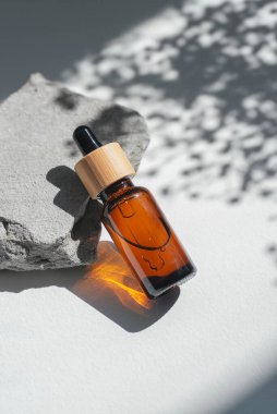 Kehribar şişelerinde serum, tonik ya da gri beton podyumda gerekli yağ var. Beyaz arka plan, gün ışığı ve gölgeler. Yüz ve vücut bakımı için güzellik konsepti