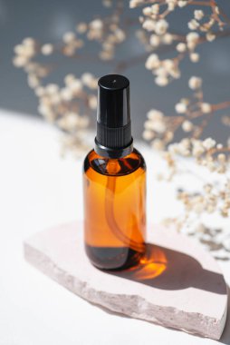 Kehribar şişesinde serum, tonik ya da esaslı yağ var. Pembe beton podyumda. Beyaz arka plan, gün ışığı ve kır çiçekleri. Yüz ve vücut bakımı için güzellik konsepti