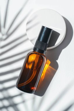Amber pump bottle with serum, tonic or essential oil on concrete podium. White background with daylight with palm shadows. Beauty concept for face and body care