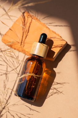 Bambu kapaklı ve kuru bitkili kehribar cam damlası. Ürün sunumu için kırmızı beton podyumda bir şişe. Cilt bakım ürünleri ve kır çiçekleri. Güzellik konsepti