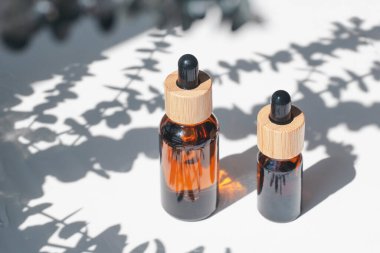 Amber bottle with dropper pipette with serum or essential oil with eucalyptus shadows. White background with daylight. Beauty concept for face and body care