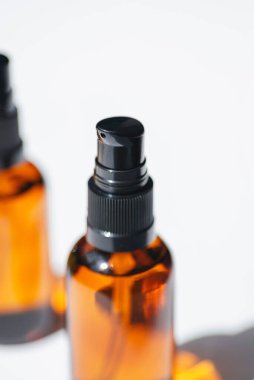 Open amber pump bottles with serum, tonic or essential oil in soft focus. White background with daylight. Beauty concept for face and body care