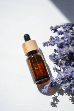 Amber dropper bottle with serum, tonic or essential oil. White background with daylight with lavender flowers. Beauty concept for face and body care