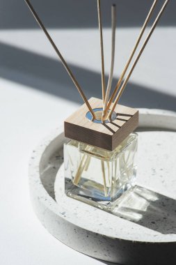 Beyaz arka planda terrazzo podyumunda şeffaf bir şişe aroma yayıcı var. Ev yapımı sunum için parfüm. Moda konsepti. Sarı sıvı ve ahşap kaplama