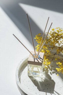Transparent bottle of aroma diffuser on the terazzo podium on white background. Eau de parfum for home presentation on a podium with field flowers. Trending concept in natural materials.