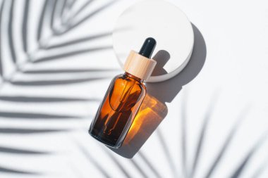Amber dropper bottles with serum, tonic or essential oil on concrete podium. White background with daylight with palm shadows. Beauty concept for face and body care