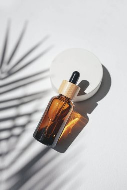 Amber dropper bottles with serum, tonic or essential oil on concrete podium. White background with daylight with palm shadows. Beauty concept for face and body care