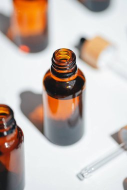 Kehribar, mavi ve şeffaf şişeler serumla kaplanmamış ya da beyaz çiçeklerle yağlanmamış. Bej arka plan, gün ışığı ve güzel gölgeler. Yüz ve vücut bakımı için güzellik konsepti