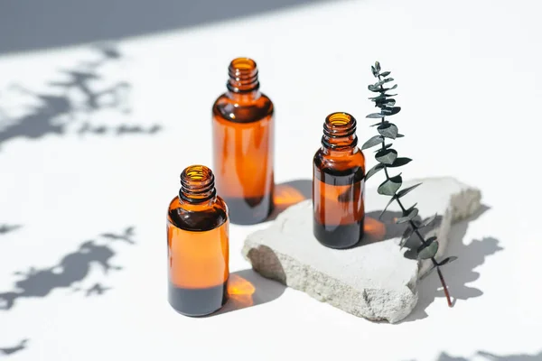 Open amber bottles without cap with eucalyptus branche. White background with daylight and beautiful shadows. Skincare serum or essential oil natural cosmetic. Beauty concept for face and body care