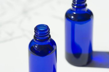 Open blue bottle with serum or essential oil. White background with daylight and beautiful shadows. Beauty concept for face and body care