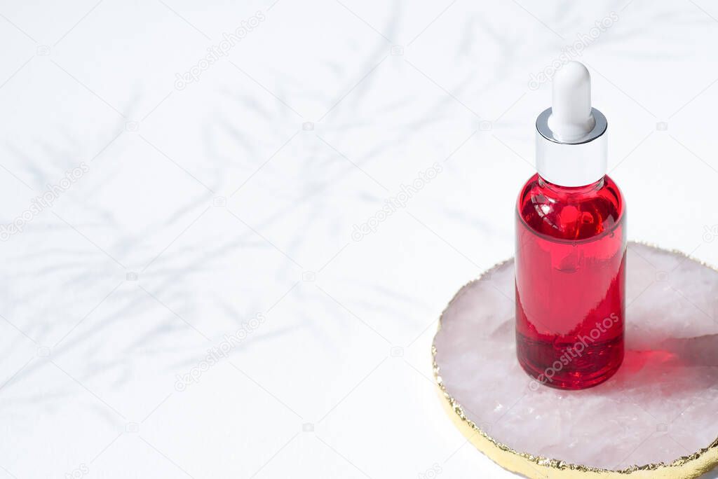 Red glass dropper bottle stone podium on white background. Skincare products, natural cosmetic. Beauty concept for face and body care.