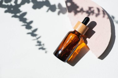 Kehribar şişesinde damlatan pipette serum ya da okaliptüs gölgeli pembe beton podyumda gerekli yağ. Gündüz vakti beyaz arka plan. Yüz ve vücut bakımı için güzellik konsepti