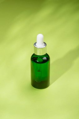 Glass bottle with dropper pipette with serum or essential oil. Green background with daylight and shadows. Skincare products , natural cosmetic. Beauty concept for face and body care