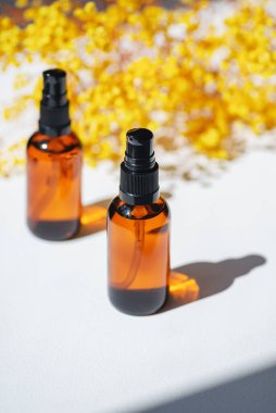 Kehribar şişeleri serumla doldurur, tonik ya da sarı çiçekli gerekli yağ. Gündüz vakti beyaz arka plan. Yüz ve vücut bakımı için güzellik konsepti