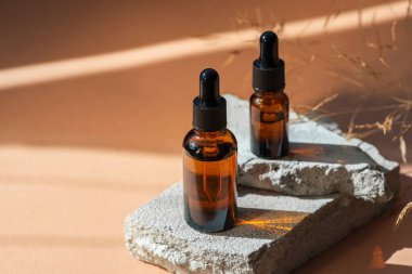 Siyah kapaklı ve kuru bitkili kehribar cam damlası. Ürün sunumu için gri beton podyumda şişeler. Cilt bakım ürünleri ve kır çiçekleri. Güzellik konsepti